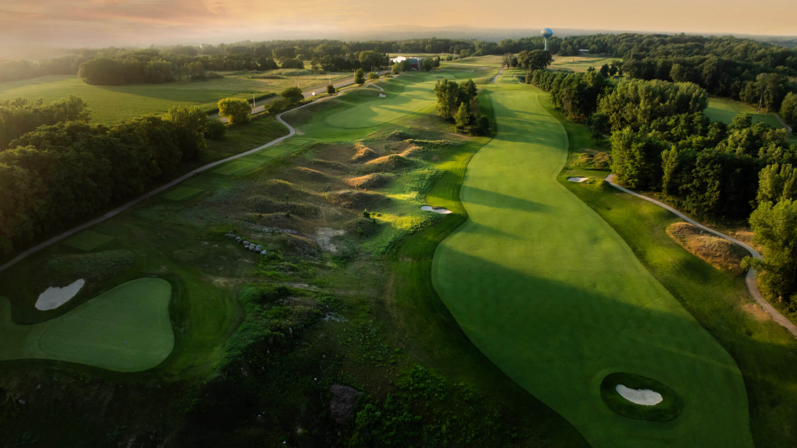 Wild Rock aerial view of holes 14,15, and 16 during scenic lighting, showing the course greens and view with the Wilderness water tower in the distance. Banner image for the website to showcase the golf course.